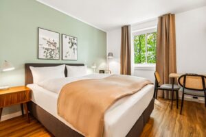 Zimmer mit einem Doppelbett und beigem Überwurf und passenden Vorhängen