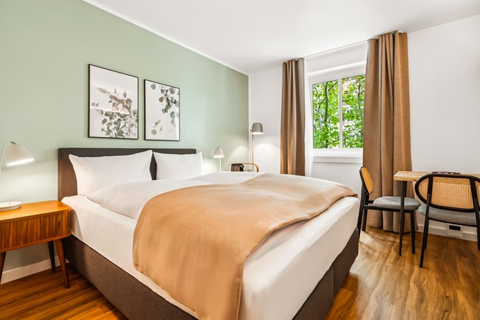 Zimmer mit einem Doppelbett und beigem Überwurf und passenden Vorhängen