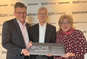 Zwei Männder und eine Frau präsentieren ein @home by Best Western-Schild