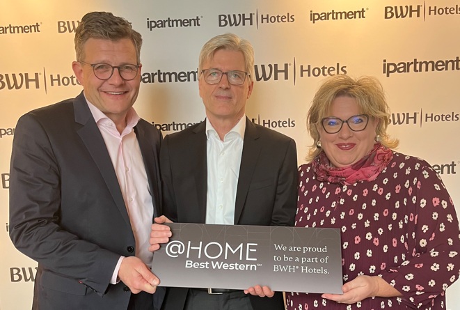 Zwei Männder und eine Frau präsentieren ein @home by Best Western-Schild