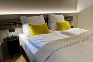 Modernes Bett in gedeckten Tönen mit gelben Kissen und Ambilight-Leiste am Kopfende