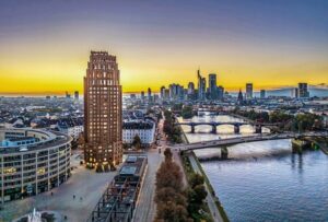 Einzelnes Hochhaus am Mainufer vor der Skyline von Frankfurt