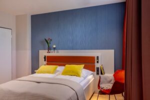 Schlafzimmer mit blauer Wand, rotem Betthaupt und gelben Kissen