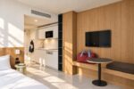 Apartment mit Küchenzeile, Bett und langer Holzwand mit Schrank, Bank und Fernseher