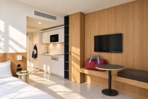 Apartment mit Küchenzeile, Bett und langer Holzwand mit Schrank, Bank und Fernseher