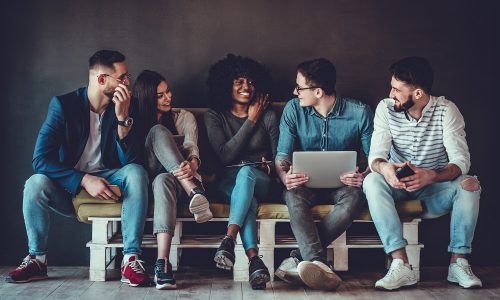 Happy diverse friends group sharing social media app news sitting holding phones, smiling multiracial young people students showing funny videos on laptop